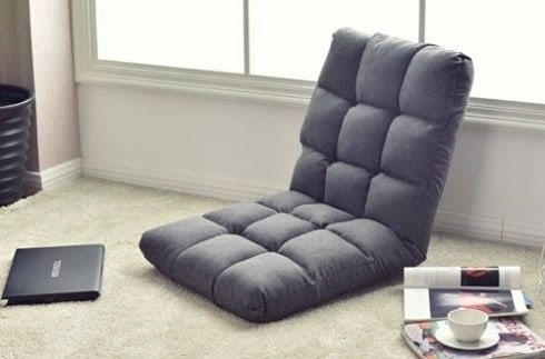 A grey floor chair, laptop, cup of coffee are on the floor