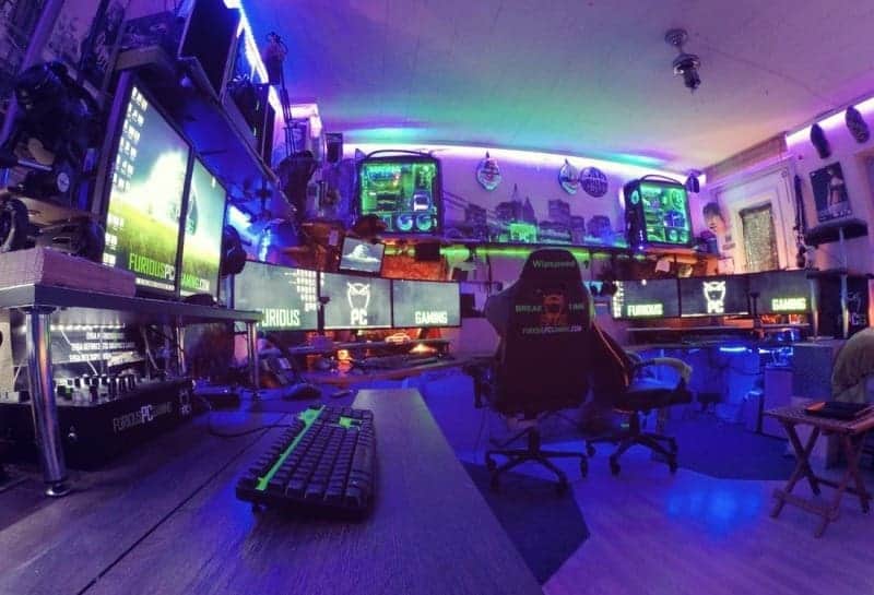 A gaming room with a lot of monitors, gaming chairs and other stuff