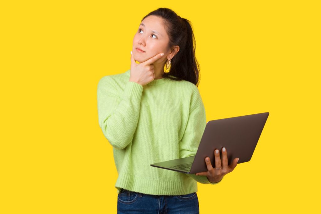 A thinking girl is touching her face while holding her laptop